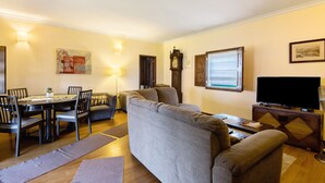 Un salon avec un canapé, une table à manger et des chaises, un téléviseur et une horloge au mur.