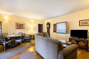 A living room with a sofa, a dining table with chairs, a television, and a clock on the wall.