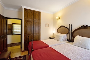 A hotel room with two beds, wooden wardrobe, and a nightstand with a lamp.