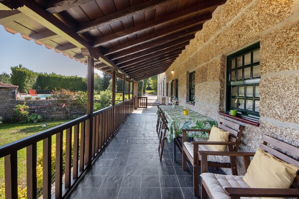 A covered outdoor area with a table and chairs, a stone wall, and a view of a garden.