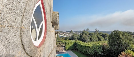 Un edificio de piedra con un emblema circular, piscina y vistas a un pueblo y vegetación.