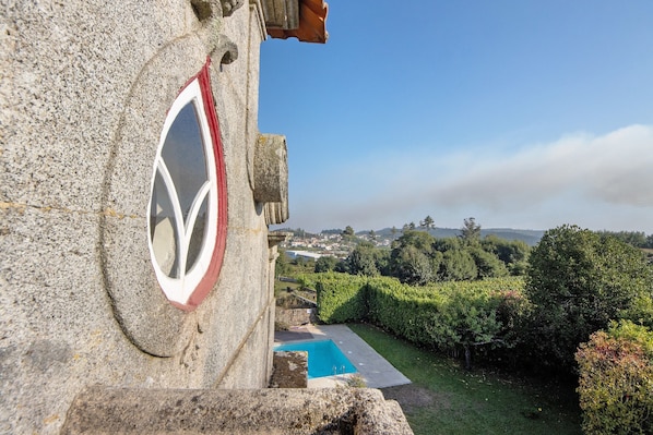 A stone building with a circular emblem, a swimming pool, and a view of a town and greenery.