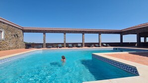 Uima-allas, jossa on kiviseinät ja laatoitettu allasterassi, ja sen ympärillä on rentoutumistuoleja sekä pergola.