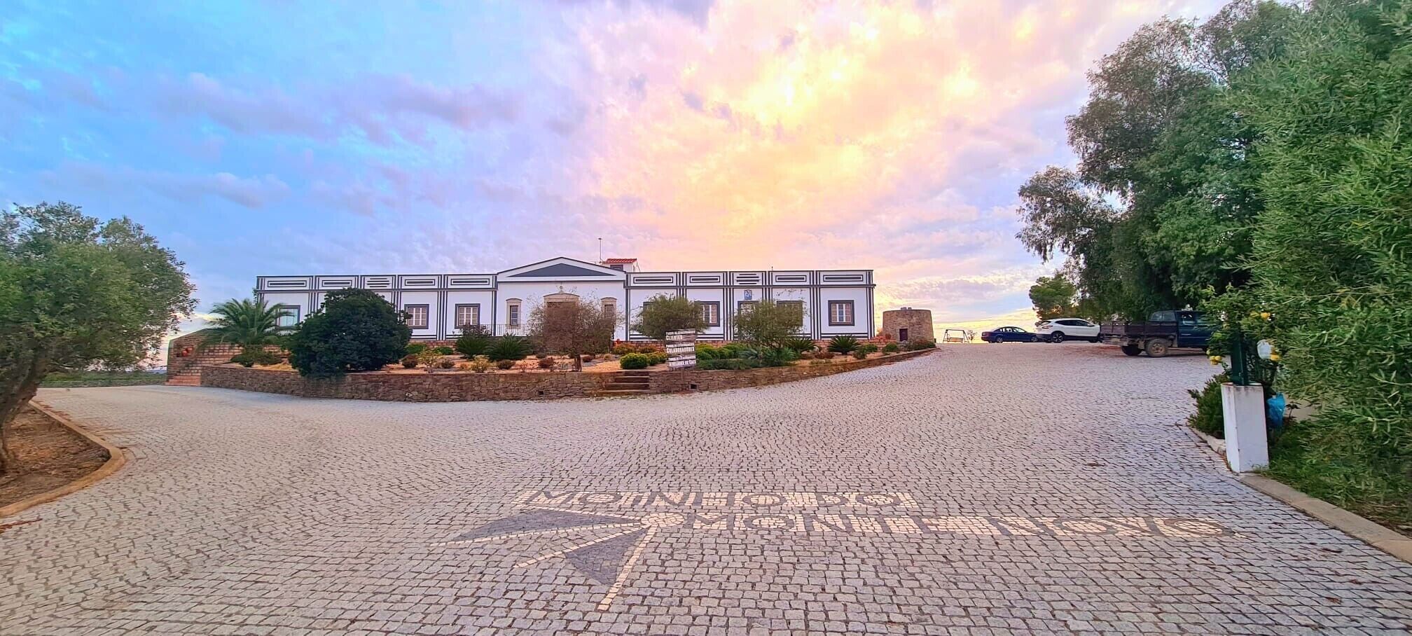 Un edificio con fachada simétrica, patio empedrado y muro de piedra.