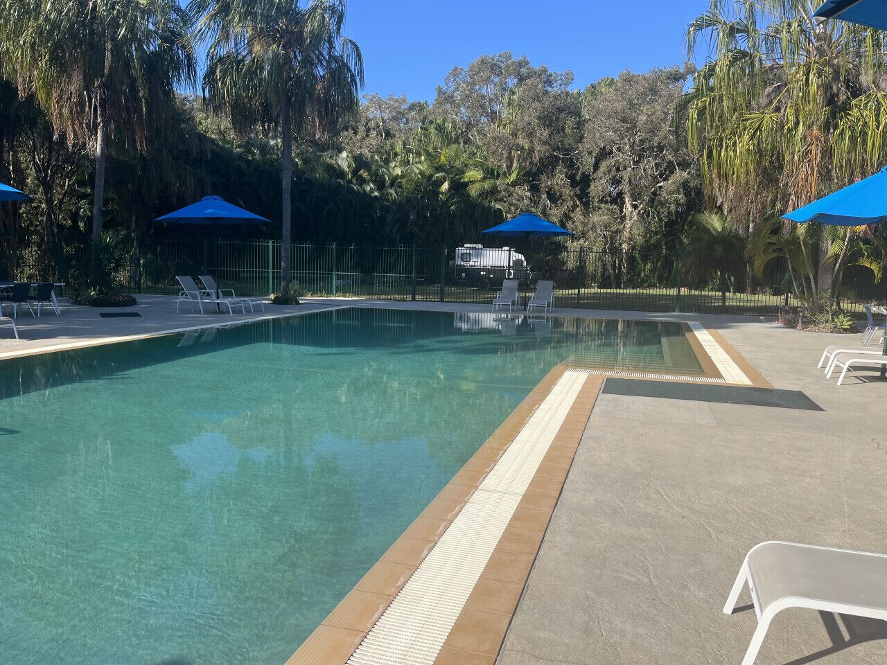 A clear swimming pool with a safety edge, surrounded by lounge chairs and umbrellas.