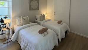 Ein Hotelzimmer mit zwei Betten, einem Deckenventilator, einem an der Wand befestigten Kunstwerk und einer Schiebetür.