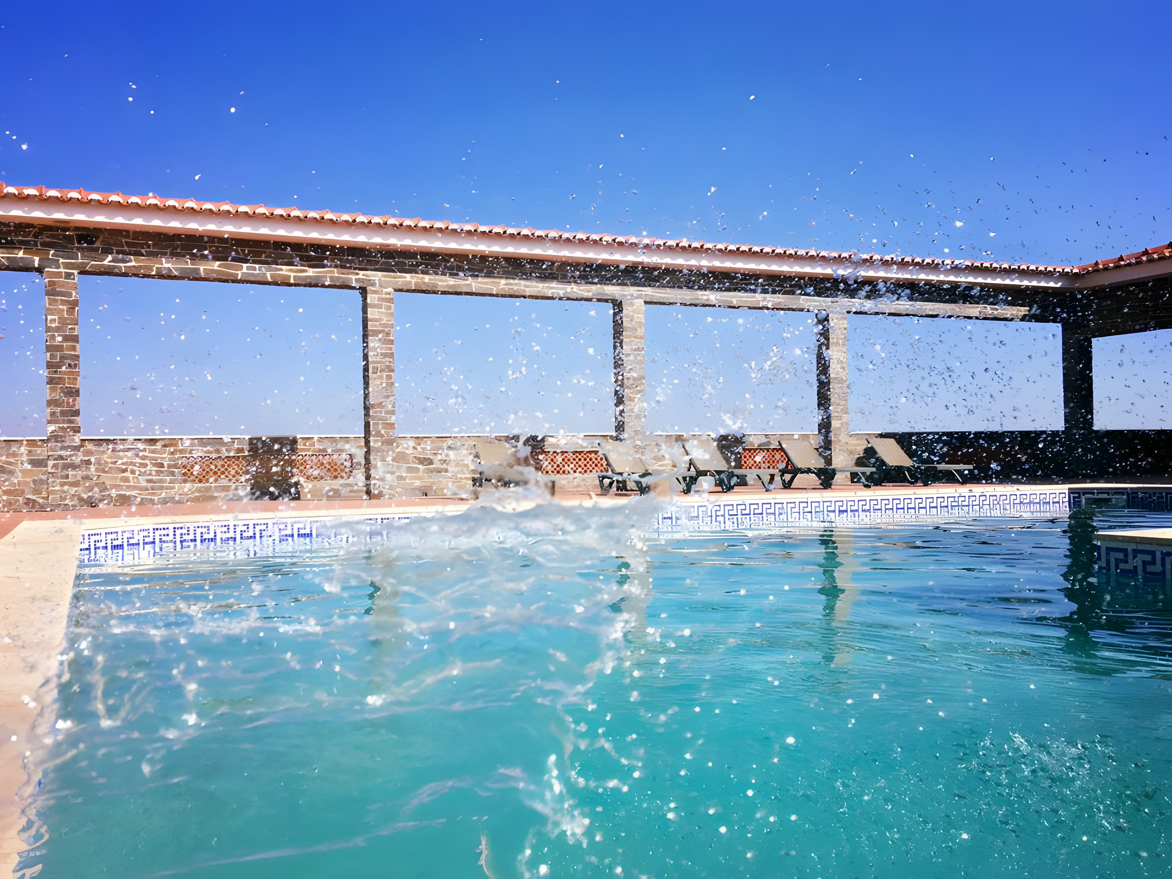 Piscina com água azul cristalina, rodeada por área coberta com telhado em azulejo e paredes de tijolo.