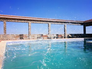 A swimming pool with clear blue water, surrounded by a covered area with a tiled roof and brick walls.