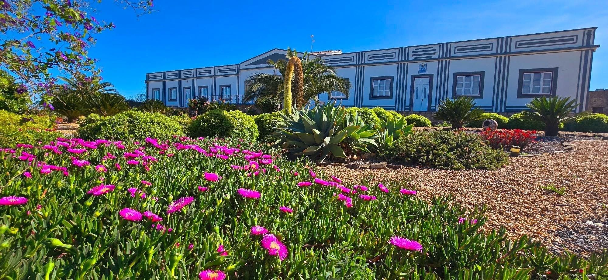 Un edificio con fachada simétrica, rodeado por un jardín ajardinado con diversas plantas y flores.