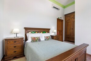 A bedroom with a wooden bed, two bedside tables, a nightstand, a wardrobe, and an air conditioning unit. - Room 'Quarto Verde - Countryside View with Patio' with Shared Pool, Wi-Fi and Air Conditioning (Moinhos de vento de cima)