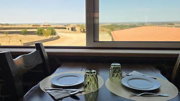 Tavolo imbandito per due con vista su un paesaggio rurale attraverso una finestra.