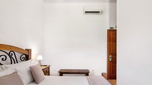 A bedroom with a bed, bedside table, lamp, and a wooden bench.