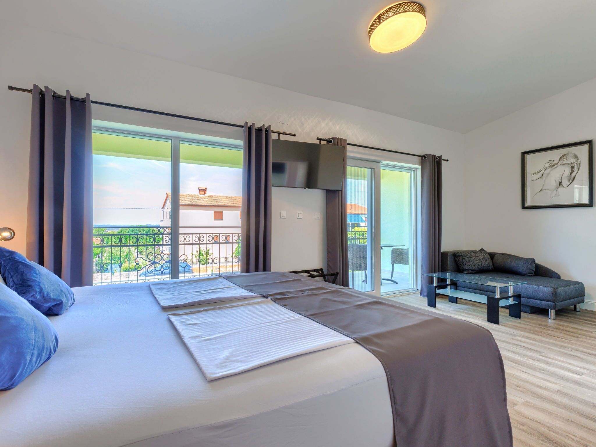 Ein Hotelzimmer mit einem großen Bett, einem Sofa, einem Balkon mit Blick und einer Deckenleuchte.