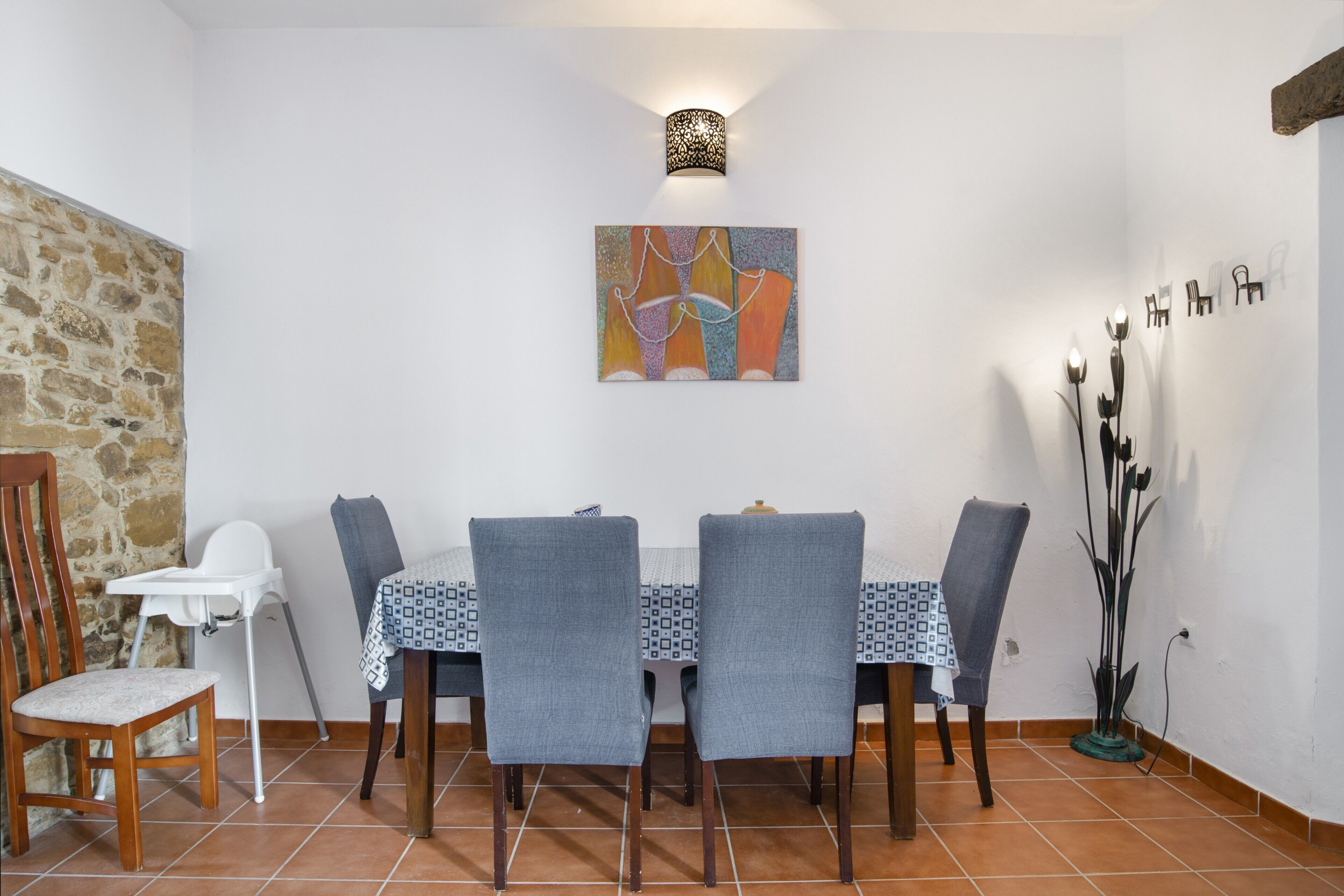 Zona pranzo con tavolo imbandito per quattro persone, seggiolino e applique a parete.