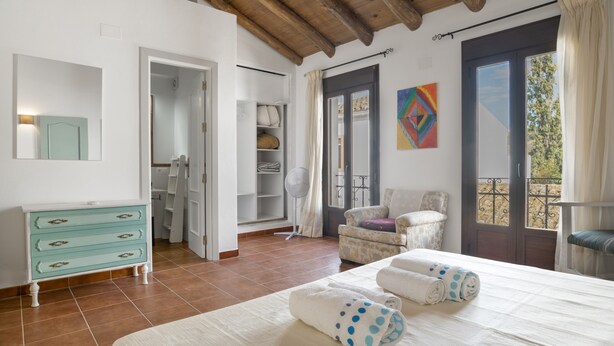 Une chambre avec un lit, une commode, une chaise et une vue sur le balcon.
