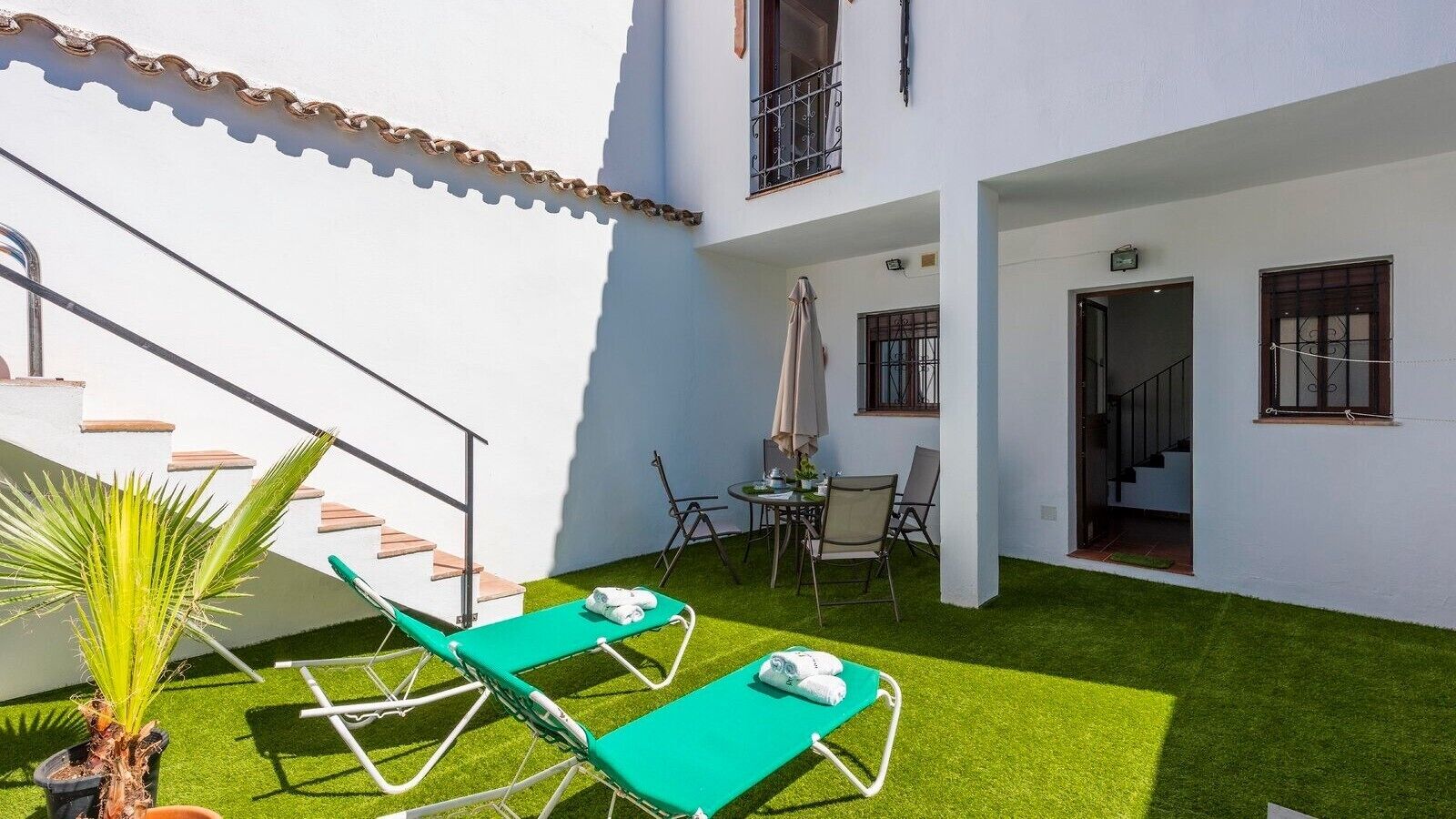 Ein Innenhof mit künstlichem Rasen, zwei grüne Lounge-Stühle, ein kleiner Tisch mit Sitzgelegenheiten und eine Treppe zu einer erhöhten Ebene.