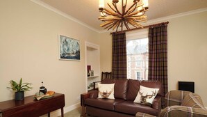 A cozy living room with a brown leather sofa, plaid curtains, a wooden coffee table, and a painting on the wall. - Downright Gabbler (Beauly)