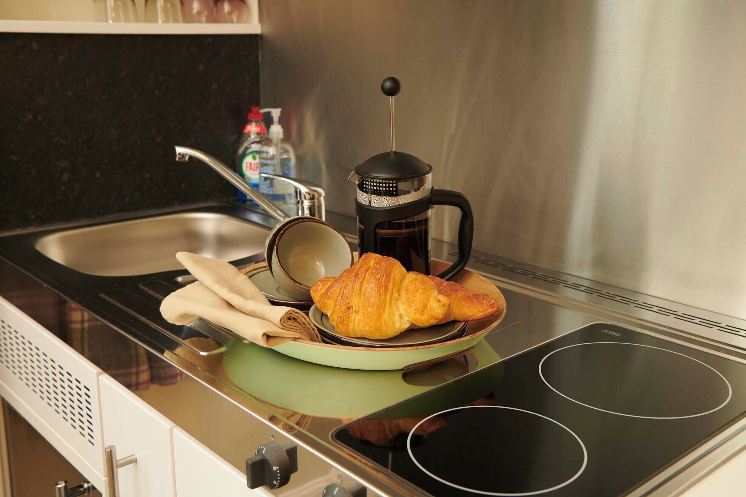 A kitchen with a stove, a coffee maker, a croissant, and a bottle of dish soap.