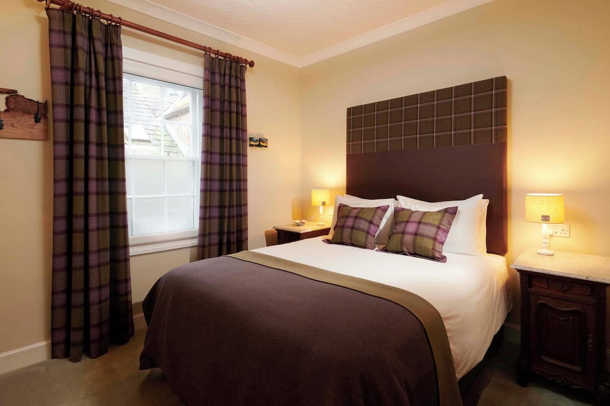 A hotel room with a large bed, two bedside tables with lamps, plaid curtains, and a window with a view of the outside.