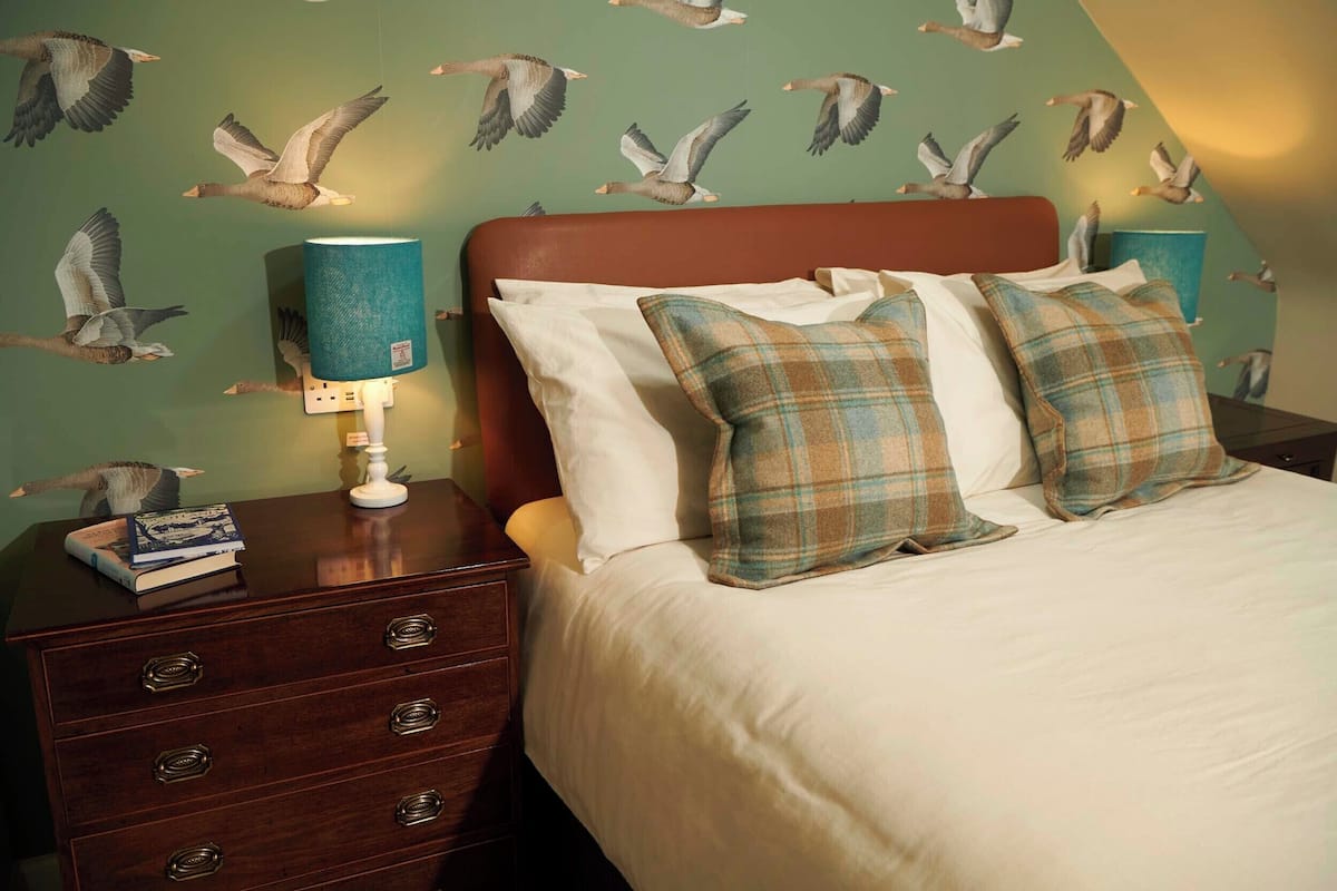 A bedroom with a bed, two pillows, a nightstand, a lamp, and a dresser.