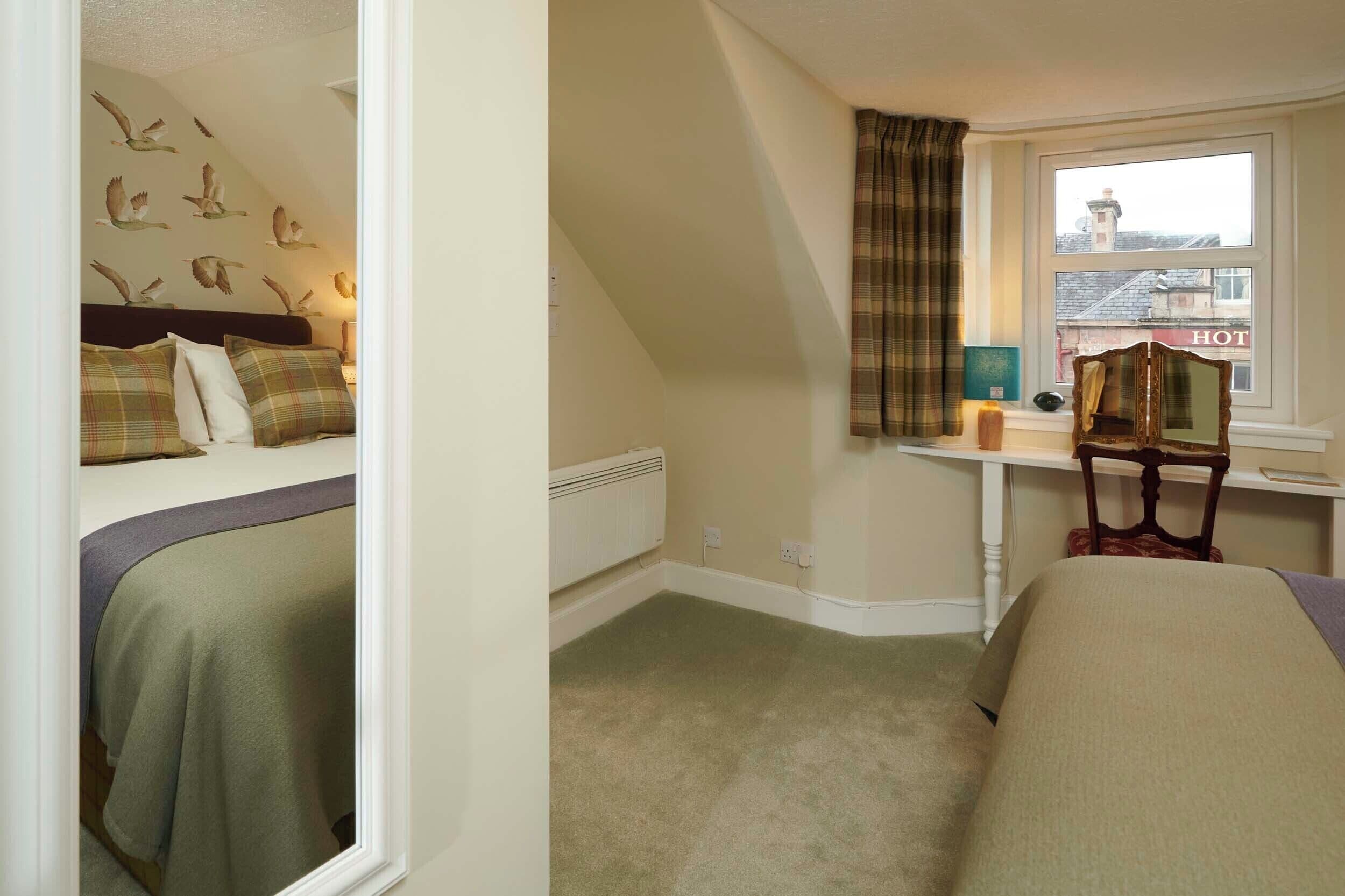 A bedroom with a bed, a desk, and a window.