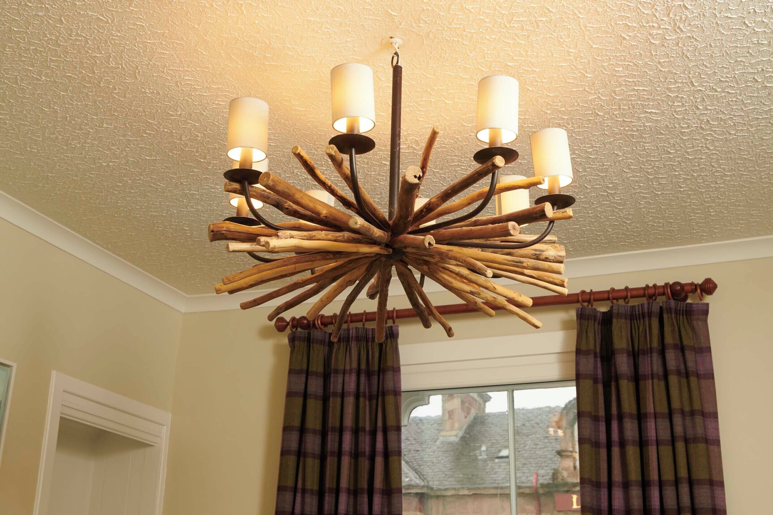 A chandelier with multiple light fixtures, a window with curtains, and a textured ceiling.