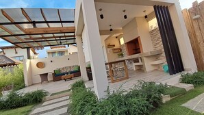 A modern outdoor living area with a covered patio, a seating area with a sofa and coffee table, and a kitchen with a stone backsplash.