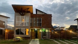 A modern two-story house with a large glass window, a wooden deck, and a well-lit entrance.