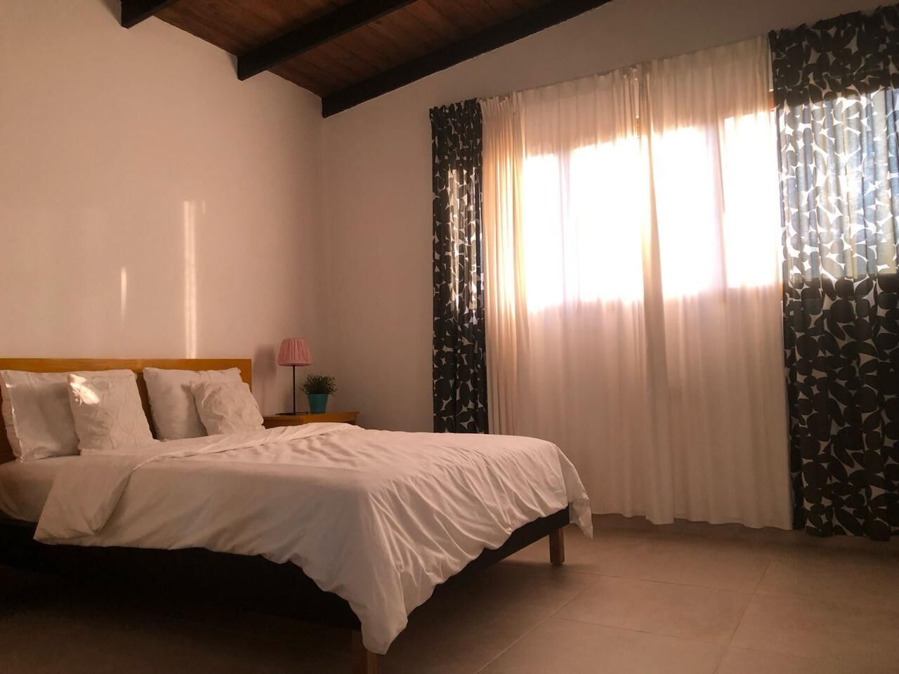 Un dormitorio con una cama, una mesita de noche, una lámpara y cortinas.