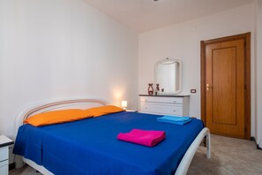 Een slaapkamer met een bed, nachtkastje, dressoir, spiegel en een houten deur.