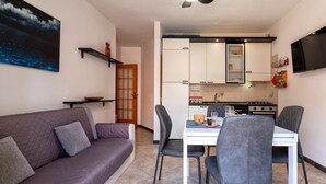Ein modernes Wohnzimmer mit einer Couch, einem Esstisch mit Stühlen, einer Küchenzeile mit Schränken und einem an der Wand befestigten Fernseher.