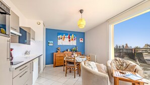 Een moderne keuken met witte kasten, een eethoek met een houten tafel en stoelen, een bank en een groot raam met uitzicht op de stad.
