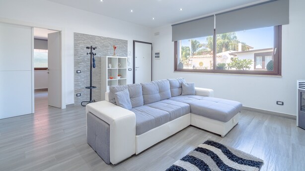 Una sala de estar moderna con un sofá seccional, una estantería empotrada, un ventanal grande y un ventilador de techo.