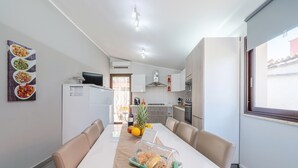 Una cocina moderna con armarios blancos, una mesa de comedor con sillas color beige y vistas al exterior por una ventana.