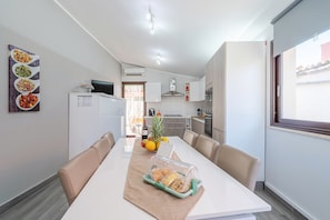 A modern kitchen with white cabinets, a dining table with beige chairs, and a view of the outside through a window.