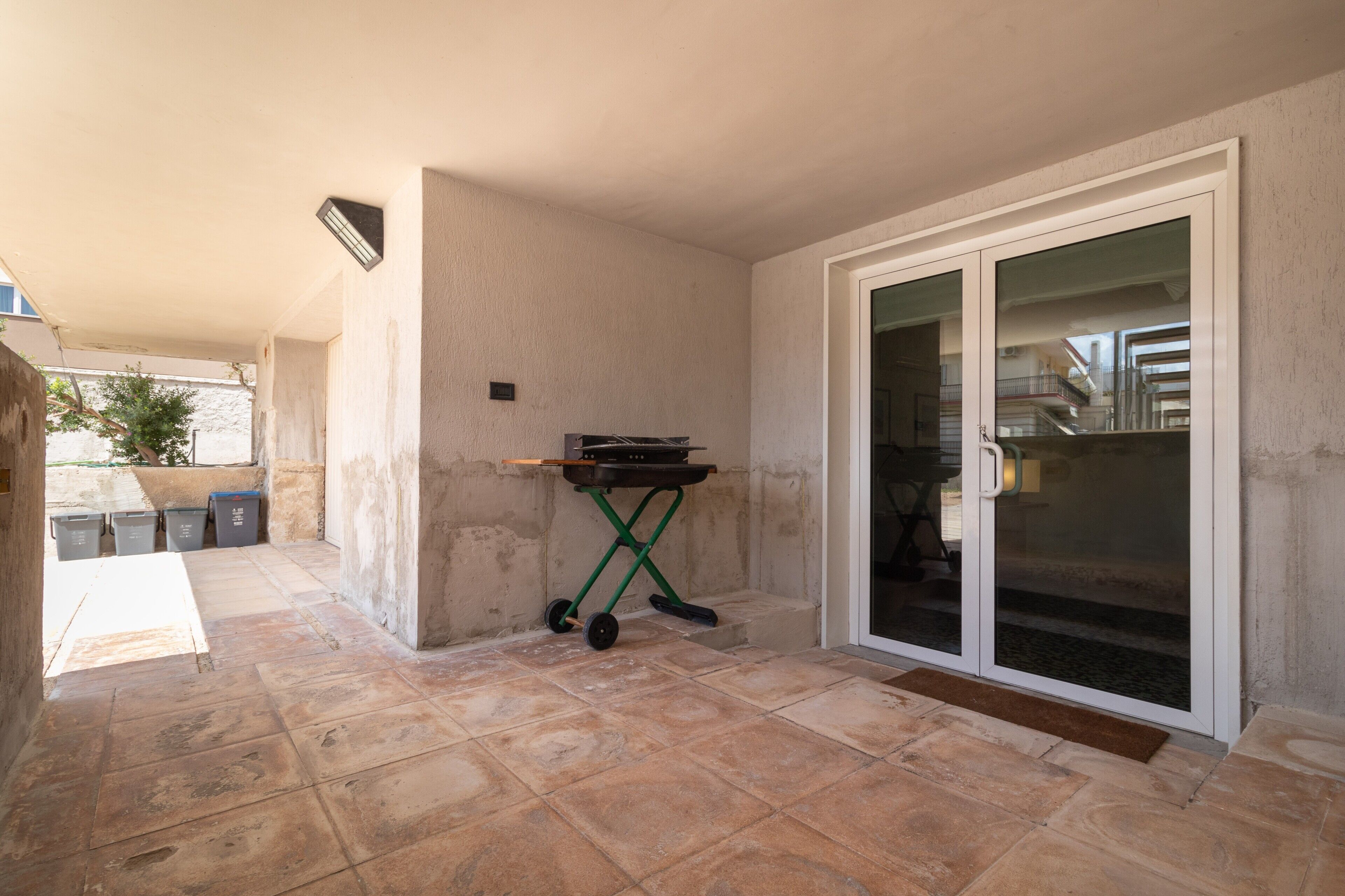 Un espace patio équipé d’un barbecue, d’une porte-fenêtre coulissante et d’un sol carrelé.