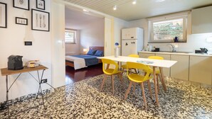 Una stanza compatta con un letto, un angolo cottura, un tavolo da pranzo con sedie gialle e un pavimento decorato.