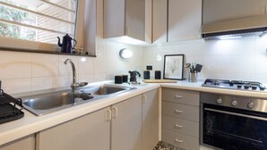 Una cucina con lavello in acciaio inox, piano cottura e finestra con persiane.