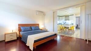 Una camera da letto con un letto di legno, comodini e vista su una sala da pranzo con sedie gialle.