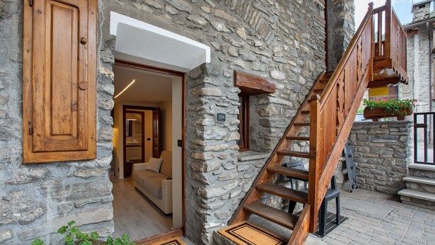 A stone building with a wooden staircase, a door, and a view into a room with a sofa. - Apartment 'Sotto' with Private Terrace and Wi-Fi (Morgex)