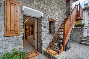 Un bâtiment en pierre avec un escalier en bois, une porte et une vue sur une pièce où se trouve un canapé.