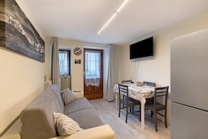 Un espace de vie compact comprenant un canapé, une table à manger, des chaises, un téléviseur à écran plat et un réfrigérateur.