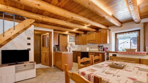 Una cocina con armarios de madera, una mesa de comedor con mantel estampado y un televisor sobre un mueble.