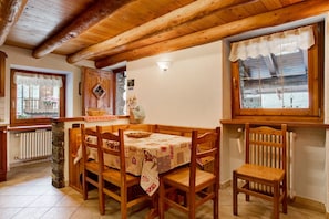 A wooden dining area with a table set for four, a stone pillar, and a window with a view of a building.