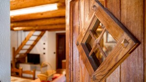 Una puerta de madera con un ventanal en forma de rombo, una escalera de madera y una mesa con mantel rojo y blanco.