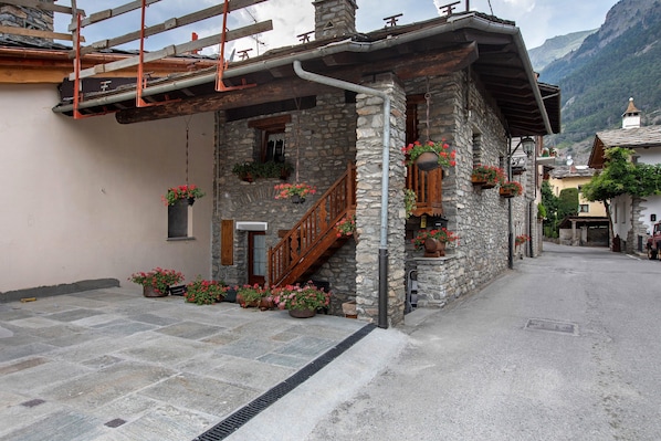A stone building with a wooden staircase, potted plants, and a metal awning.