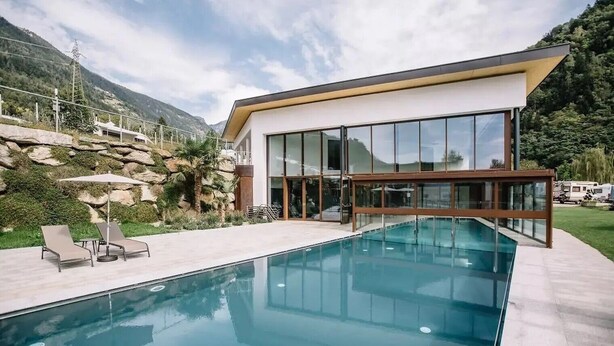 A modern house with a swimming pool, large windows, and a view of mountains.
