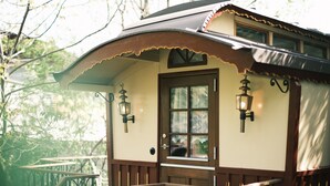 A small, wooden cabin with a porch, two wall-mounted lanterns, and a door with a window.