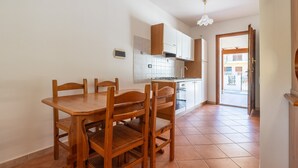 Een keuken met een eettafel en stoelen, een fornuis, kastjes en een uitzicht door een geopende deur.