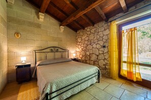 A bedroom with a stone wall, a wooden ceiling, a bed with a metal frame, two bedside tables with lamps, and a window with curtains. - Room 'Masseria Copertini - Angelo' with Wi-Fi and Air Conditioning (Vernole)